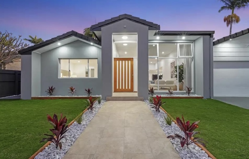 A grey rendered home with a timber front door, freshly painted, lit up at dusk