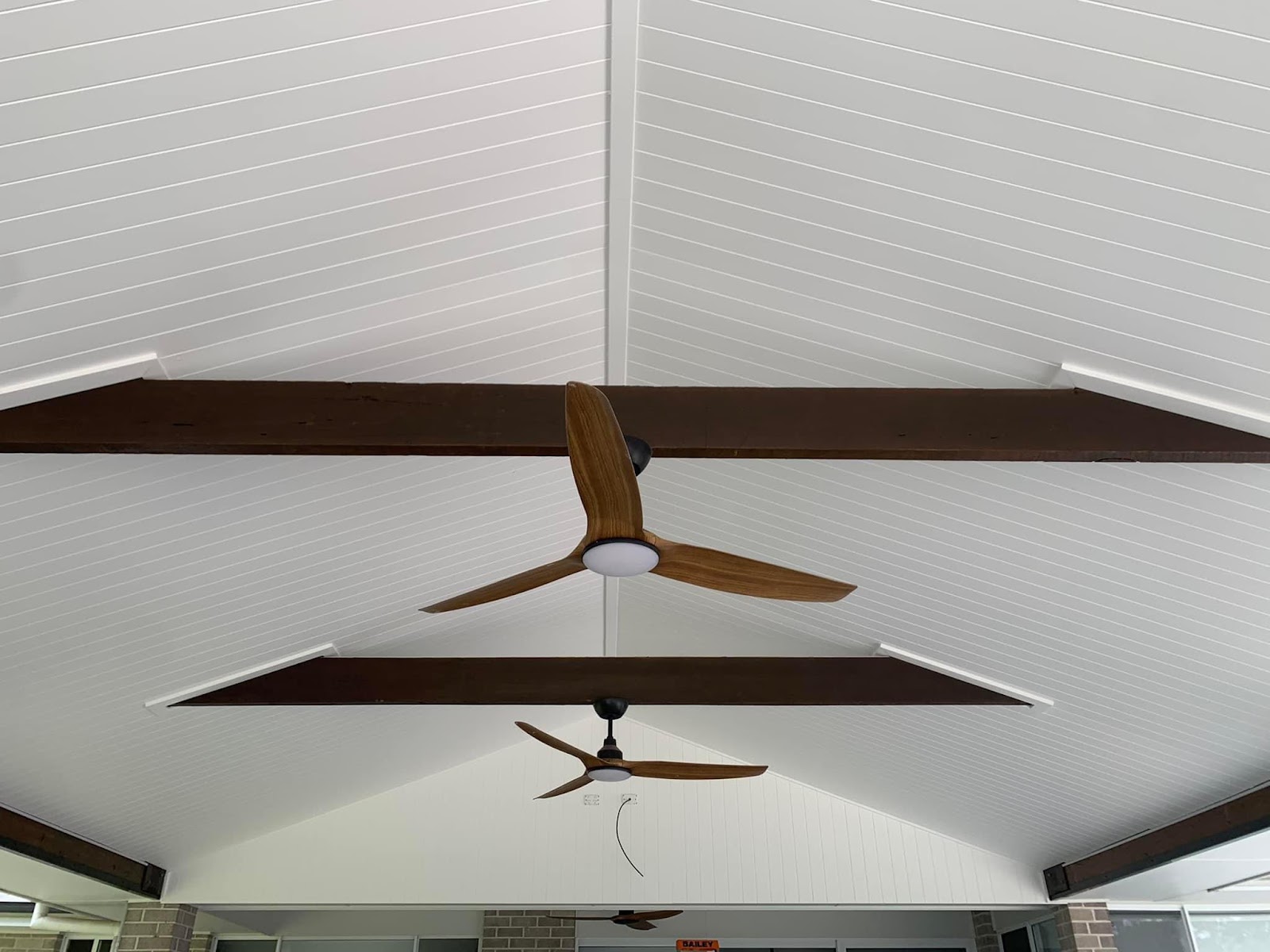 White lined ceiling with dark timber beams and ceiling fans in an outdoor room